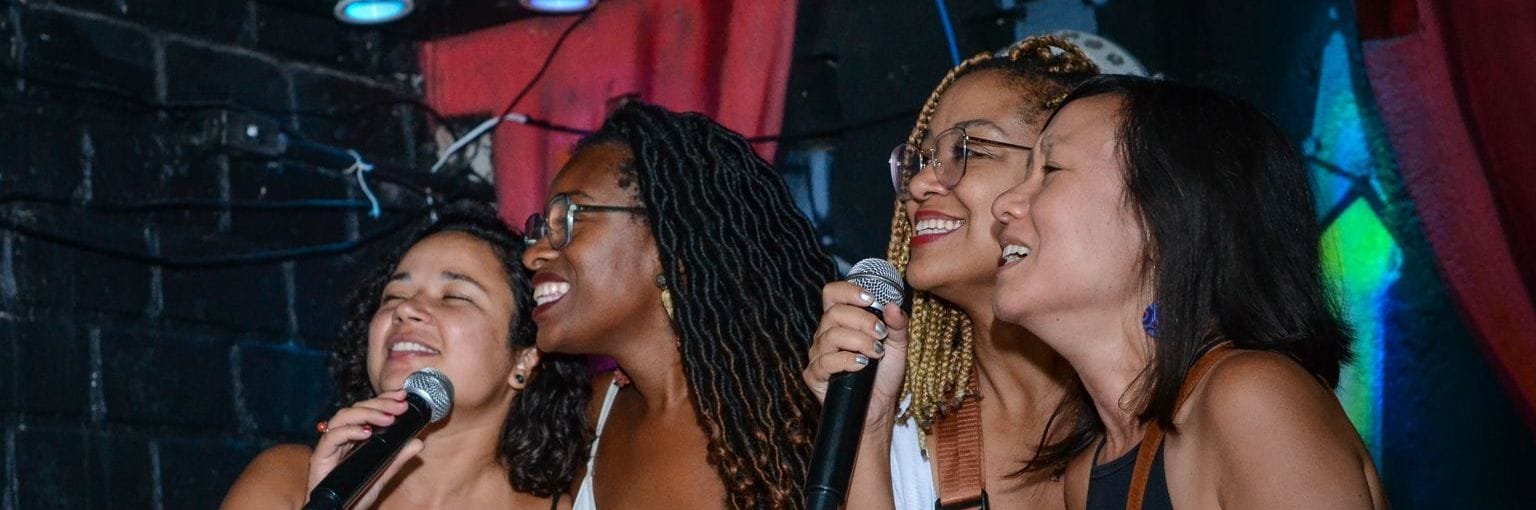 Quatro amigas cantando juntas no palco de karaokê do Graffiti