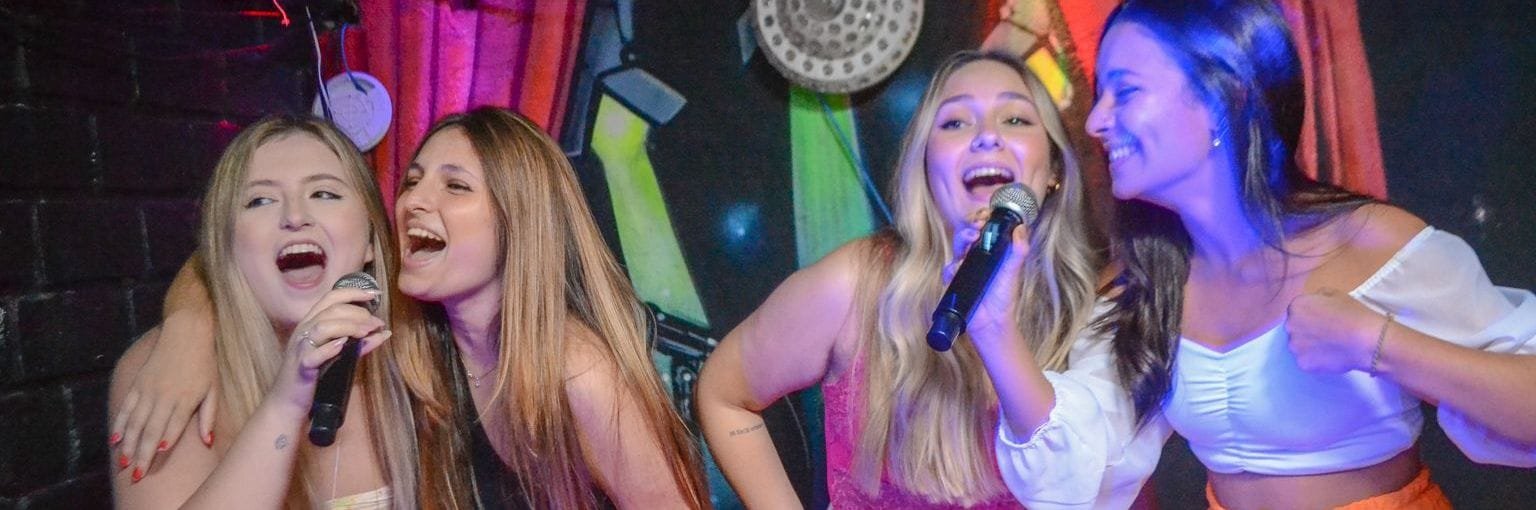 Amigas cantando karaokê juntas no palco do Graffiti